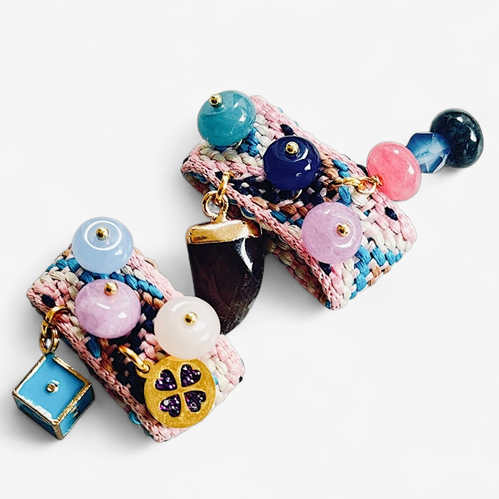 Paire de sandalinettes pastel rose et bleu avec perles violettes, blanches et bleu nuit, accompagnée de pendentifs : corne noire brillante, cube bleu et trèfle violet.