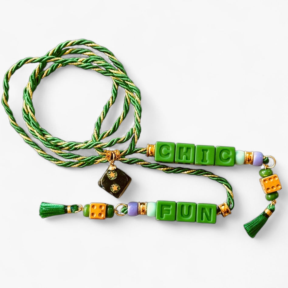 Collier Casino Club vert prairie avec lettrage “CHIC FUN”, dés dorés, perles violettes et pompons verts.