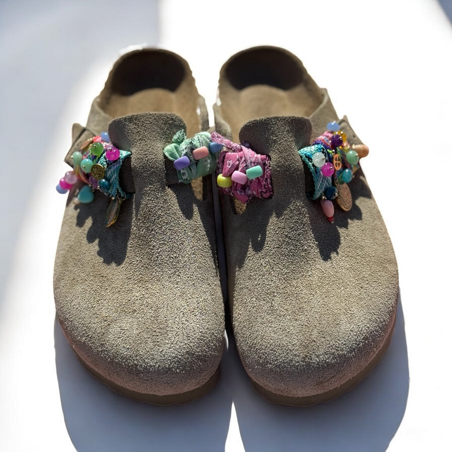 Vue de face de Birkenstock beiges décorées avec plusieurs Sandalinettes colorées, grigris et rubans tressés.