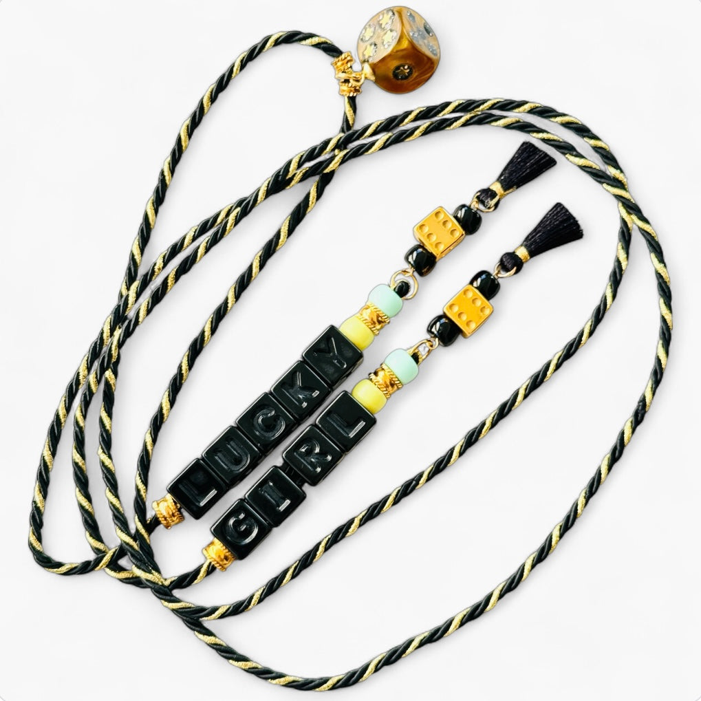 Collier Casino Club noir et doré avec lettres “LUCKY GIRL”, dés jaune or, pompons noirs et pendentif à strass.
