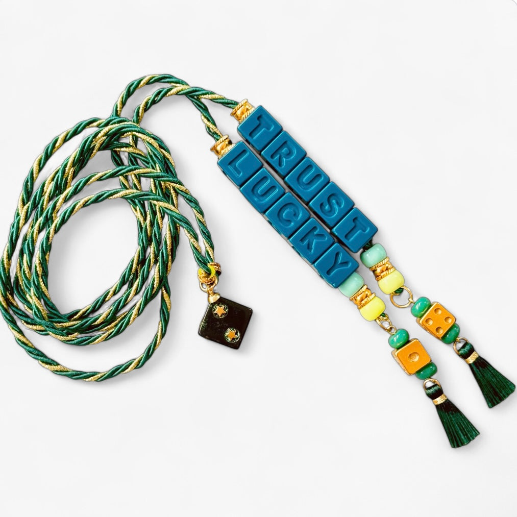 Collier Casino Club vert et doré avec message “TRUST LUCKY”, perles vertes et jaunes, dés orange et pampilles foncées.