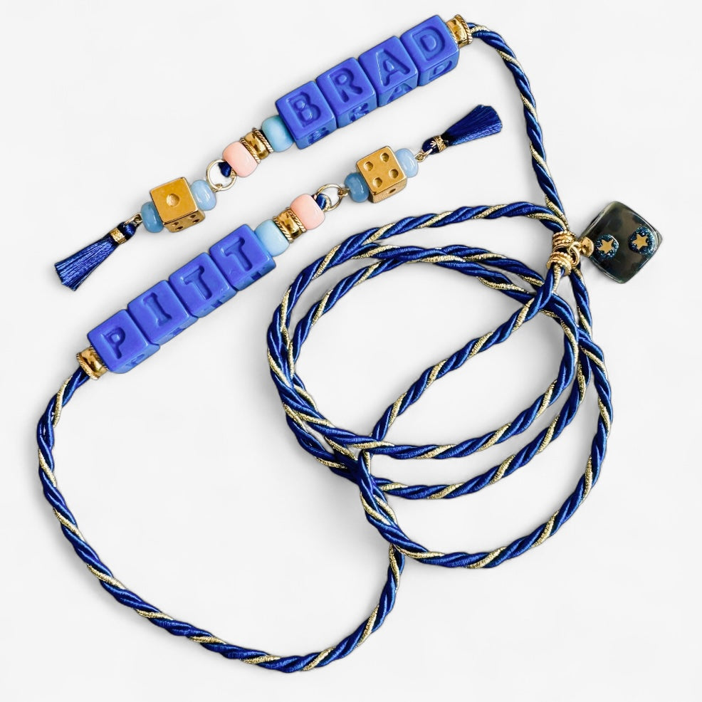 Collier Casino Club bleu royal avec lettrage “PITT BRAD”, détails dorés, perles pastel et pompons bleu marine.