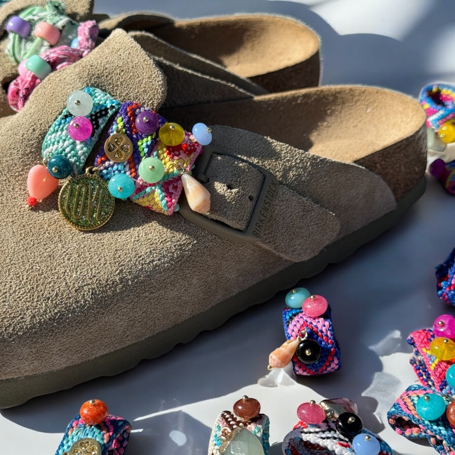 Gros plan sur les bijoux de sandales Sandalinettes tressés et perlés accrochés sur des Birkenstock en daim beige.