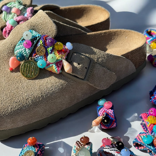 Gros plan sur les bijoux de sandales Sandalinettes tressés et perlés accrochés sur des Birkenstock en daim beige.