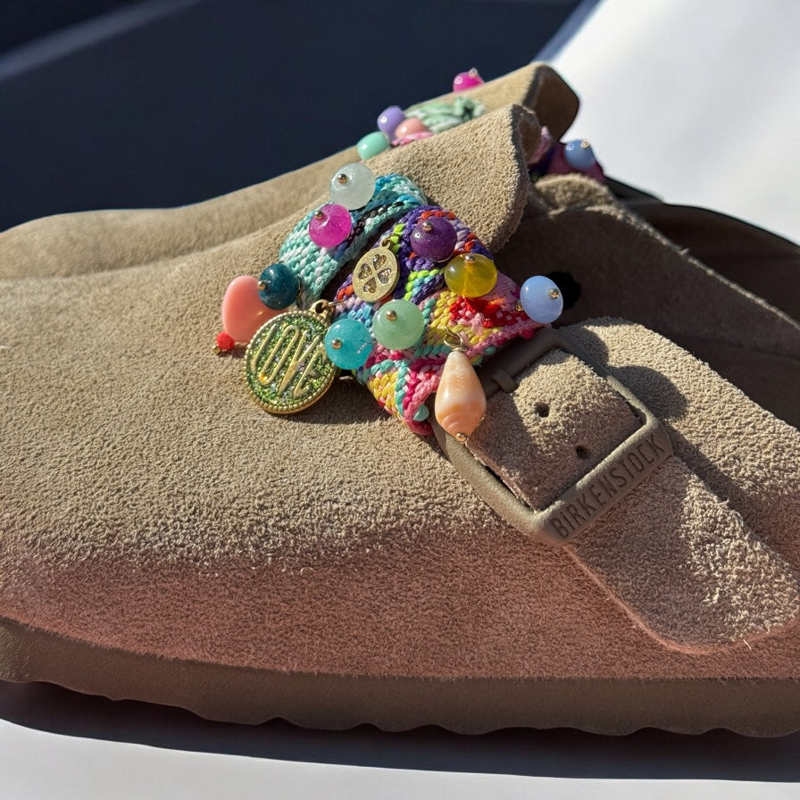Bijoux Sandalinettes en gros plan sur boucle de sandale, avec médaillon LOVE, coquillage et pierres multicolores.
